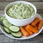 bowl of spinach artichoke dip with sliced cucumbers and carrots around the bowl