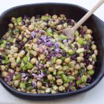 Bean salad ins side a ceramic black bowl with a wooden spoon