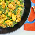 A blue skillet filled with turmeric-seasoned chicken and green asparagus with a bright red napkin