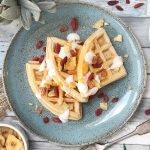 Three waffles stacked on a blue plate with gogi berries and coconut