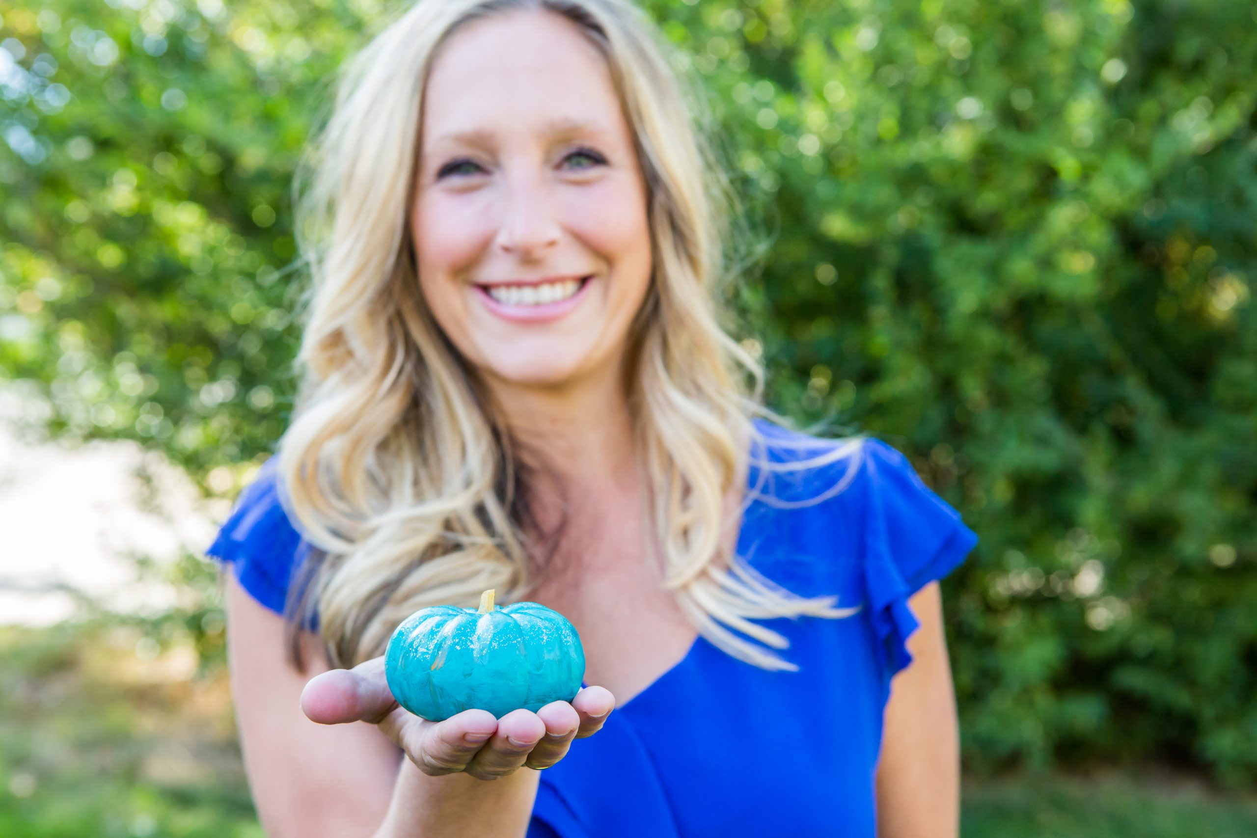Blond woman holding teal pumpkin in her palm outdoors
