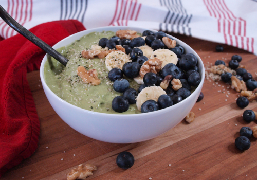 white bowl with green smoothie inside topped with berries, bananas and nuts