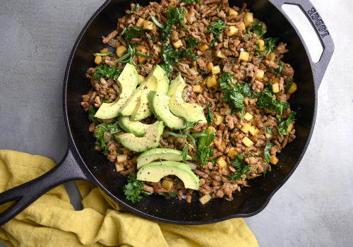 cast iron skillet with ground turkey, veggies and topped with sliced avocado