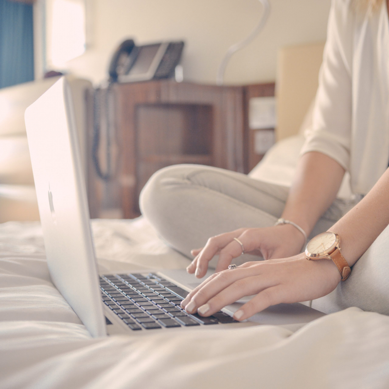Woman on her bed with her legs crossed typing on a laptop