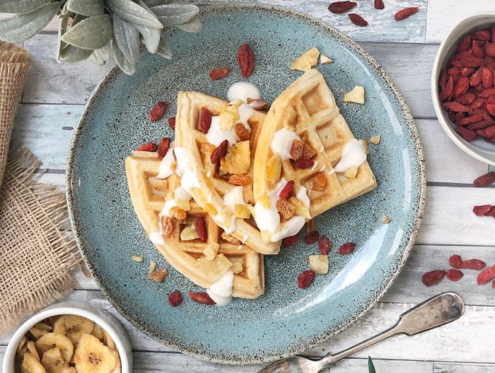 Three waffles stacked on a blue plate with gogi berries and coconut