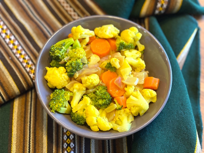 A bowl of broccoli, cauliflower, and chopped carrots in a yellow curry sauce.