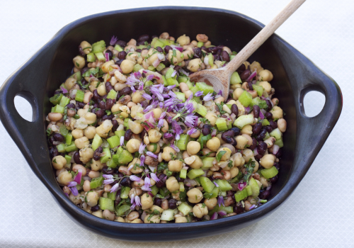 Bean salad ins side a ceramic black bowl with a wooden spoon