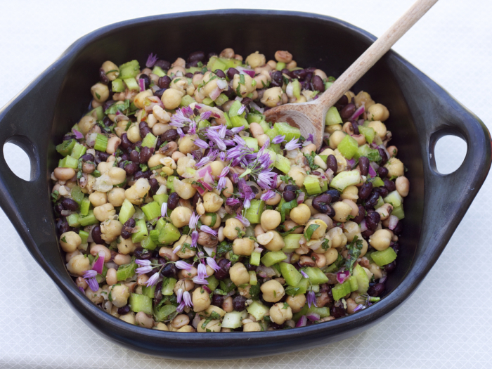 Bean salad ins side a ceramic black bowl with a wooden spoon