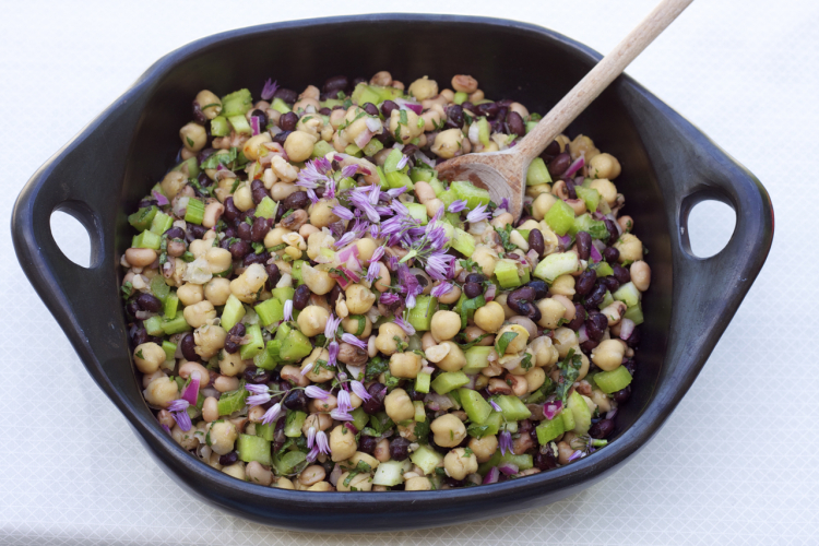 Bean salad ins side a ceramic black bowl with a wooden spoon