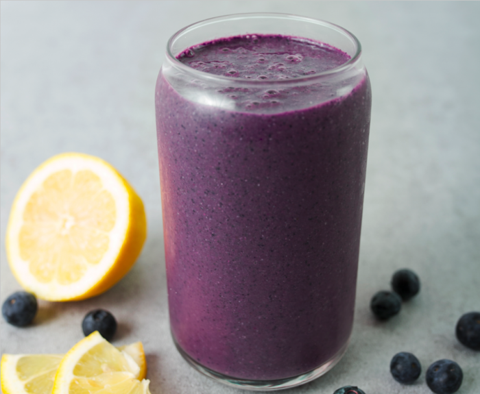 a purple smoothie within a glass jar with lemons and blueberries around