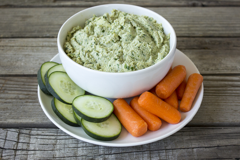 bowl of spinach artichoke dip with sliced cucumbers and carrots around the bowl