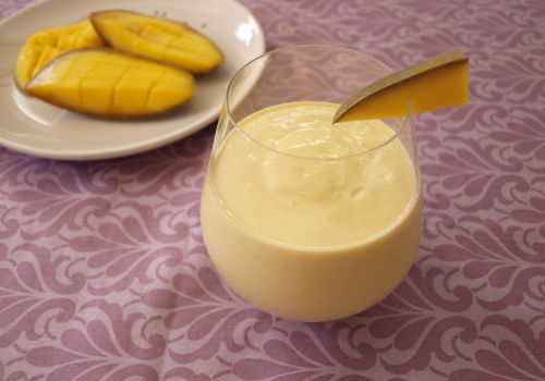 stemless wine glass with mango lassi inside and slice of mango as garnish