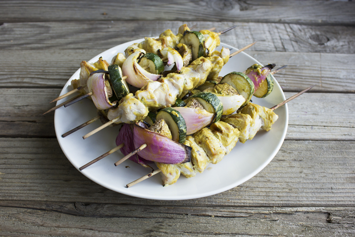 a stack of kabobs with chicken, zucchinis, red onions on a white plate on a wooden board